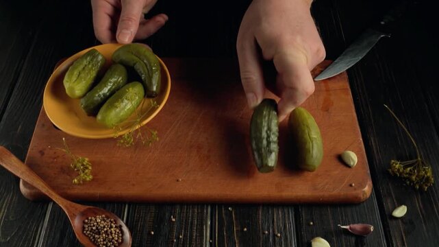 Hands of a person transferring pickles from a bowl to a wooden cutting board, showcasing the process of preparing ingredients for a meal
