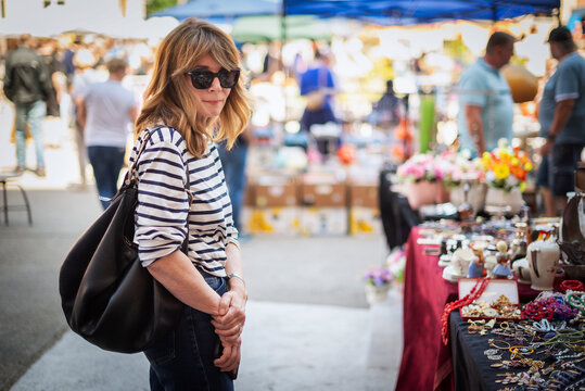 Stylish midlife woman browsing items at outdoor flea market on a sunny day