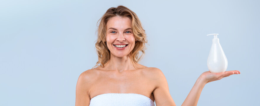 Smiling Young Caucasian Woman Holding A Bottle Of Skincare Product In An Indoor Studio Setting. Cheerful Female Engaged In Selfcare Routine, Promoting Natural Beauty And Wellness Concept