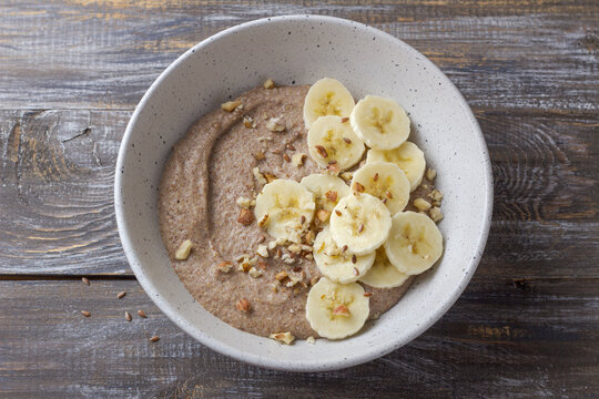 Healthy flaxseed porridge topped with banana slices, chopped nuts and seeds in a ceramic bowl. Nutritious breakfast with natural ingredients, top view