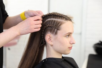 Naklejka premium Hairstylist braiding teenage girl's hair in salon, closeup