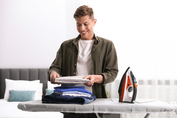 Fototapeta premium Man stacking clean clothes on ironing board at home