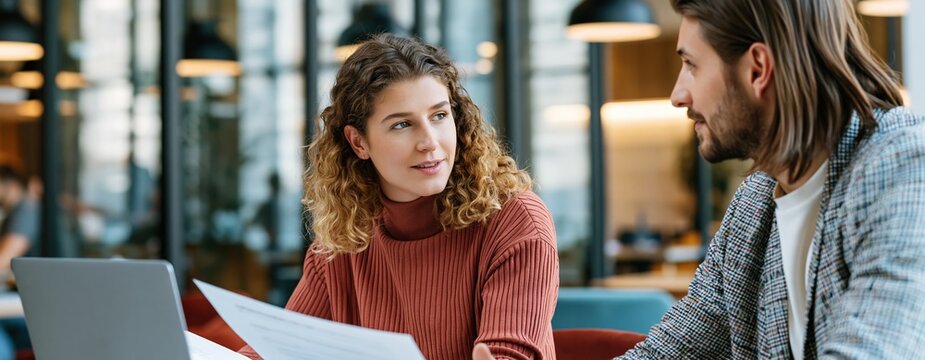 Young couple discussing documents on laptop in cozy cafe