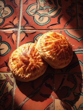 Warm morning caf&eacute; scene with traditional Maltese pastizzi pastries on a rustic table with terracotta tiles.