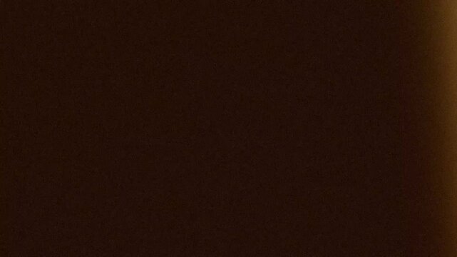 Abstract dark brown grainy texture shifting with subtle movement and warm glow in cinematic minimalist atmosphere with gritty retro film grain aesthetic