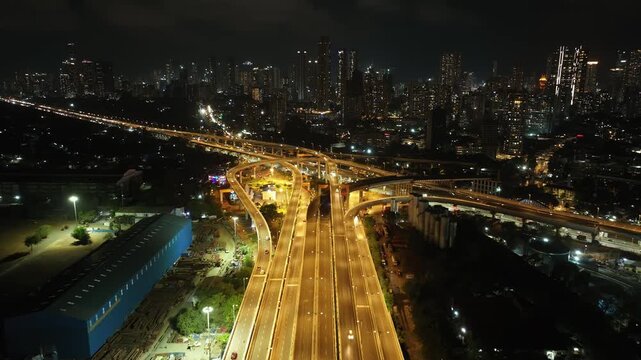 A stunning aerial night view of Atal Setu (Mumbai Trans Harbour Link), showcasing the intricate network of illuminated flyovers and highways glowing in golden light.