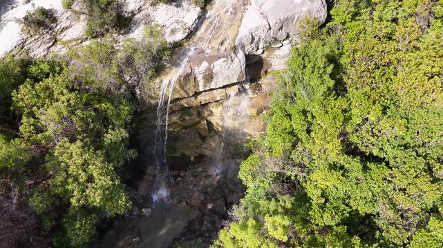 Aerial tracking shot pulling back directly from a cascading mountain waterfall near the historic Kadiut Bridge, revealing smooth limestone rock shelves and surrounding wild green brush