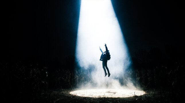 Person levitating in a beam of light from a UFO in a cornfield at night with smoke and fog