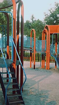 Kids enjoy their time at a park with a slide and climbing equipment. Green trees surround the area. The sun is shining on a warm afternoon as families gather.
