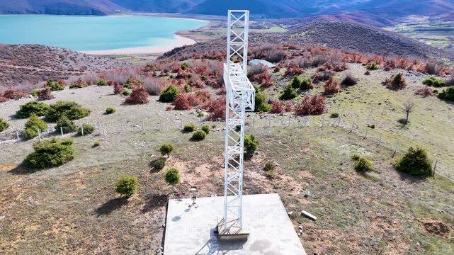 Aerial tracking shot circling a large white steel lattice cross monument on a hilltop, revealing the turquoise waters of Debar Lake and the Macedonian landscape