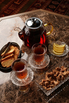 Traditional armudu glasses with black tea, teapot, lemon slices, jam, nuts, dried fruits, and sugar cubes on a table. Authentic eastern hospitality and tea culture concept