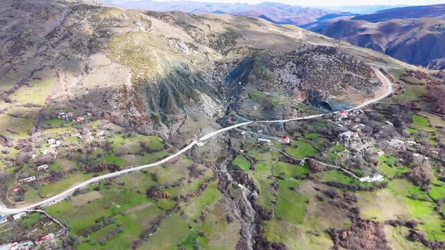 Aerial drone camera moving forward high over Uzuntas village and Arhalan Mezrasi in Poturge, Turkey, revealing a winding mountain road, rural houses, and rocky slopes