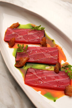 Top view of elegant tuna tataki slices served with citrus wedges, green herb oil, and ponzu sauce on an oval plate over a marble table. Gourmet seafood appetizer in a fine dining restaurant.