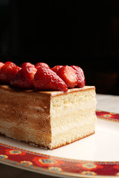 Close-up of a gourmet baked Alaska or meringue dessert topped with fresh juicy strawberries, served on an elegant red patterned platter over a marble table. Luxury restaurant sweet pastry