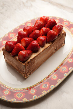 Close-up of a gourmet baked Alaska or meringue dessert topped with fresh juicy strawberries, served on an elegant red patterned platter over a marble table. Luxury restaurant sweet pastry