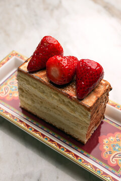 Close-up of a gourmet baked Alaska or meringue dessert topped with fresh juicy strawberries, served on an elegant red patterned platter over a marble table. Luxury restaurant sweet pastry