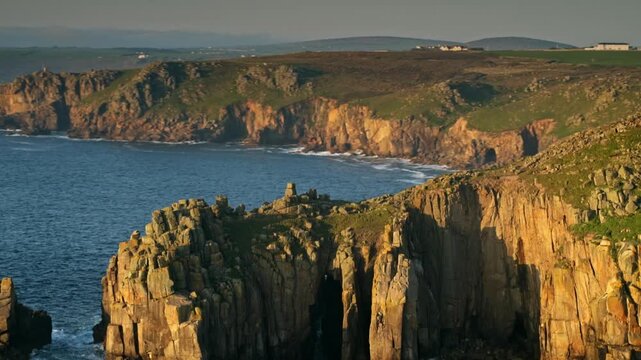 Warm sunset light casting long shadows across the dramatic, rugged coastline of Land's End, Cornwall
