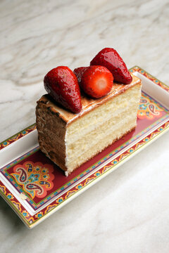 Close-up of a gourmet baked Alaska or meringue dessert topped with fresh juicy strawberries, served on an elegant red patterned platter over a marble table. Luxury restaurant sweet pastry