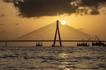 Obraz premium A breathtaking sunset view of the iconic Bandra-Worli Sea Link in Mumbai, captured in perfect silhouette against a glowing golden sky.