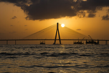 Obraz premium A breathtaking sunset view of the iconic Bandra-Worli Sea Link in Mumbai, captured in perfect silhouette against a glowing golden sky.