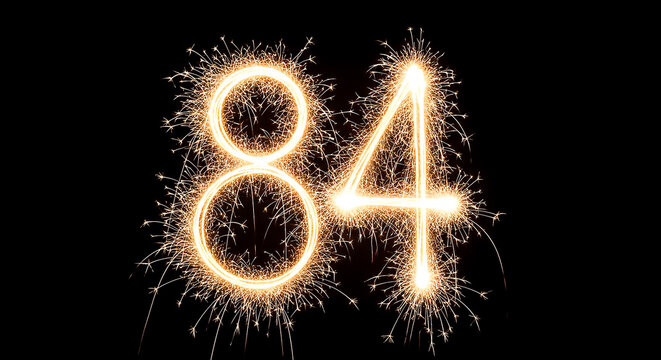 Dramatic firework sparklers create glowing numbers 84 on a pitch-black backdrop, evoking celebration and nostalgia.