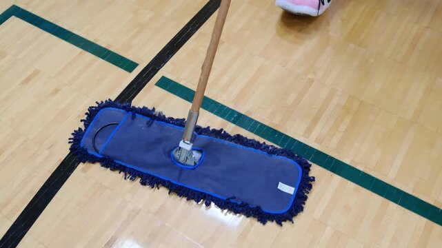 Janitor cleaning gymnasium hardwood basketball court floor