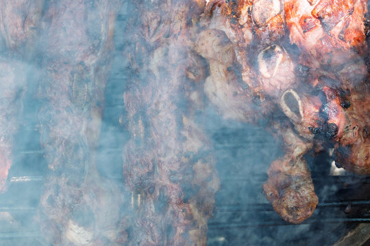 Costillas de carne vacuna cocin&aacute;ndose lentamente sobre parrilla durante proceso de asado argentino