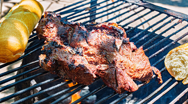 Costillas de carne vacuna cocin&aacute;ndose lentamente sobre parrilla durante proceso de asado argentino