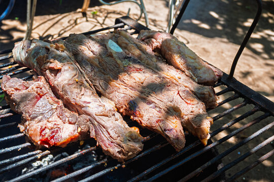 Costillas de carne vacuna cocin&aacute;ndose lentamente sobre parrilla durante proceso de asado argentino