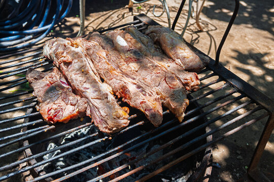 Costillas de carne vacuna cocin&aacute;ndose lentamente sobre parrilla durante proceso de asado argentino