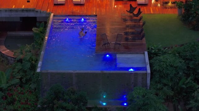 This aerial view shows a happy family enjoying their home pool in beautiful Costa Rica, surrounded by vibrant greenery and soft evening lights, creating a peaceful ambiance