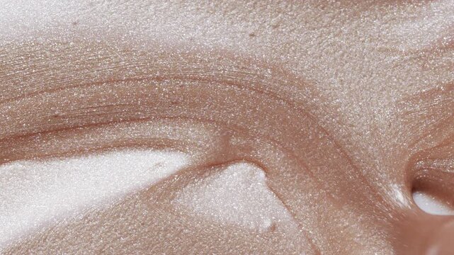 Close up of white spatula playing with golden shimmering lip gloss texture, satisfying make up gold lipgloss strokes. Cosmetic product swatch background