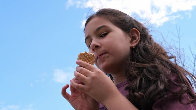 Girl biting into an ice cream cone outdoors against a blue sky