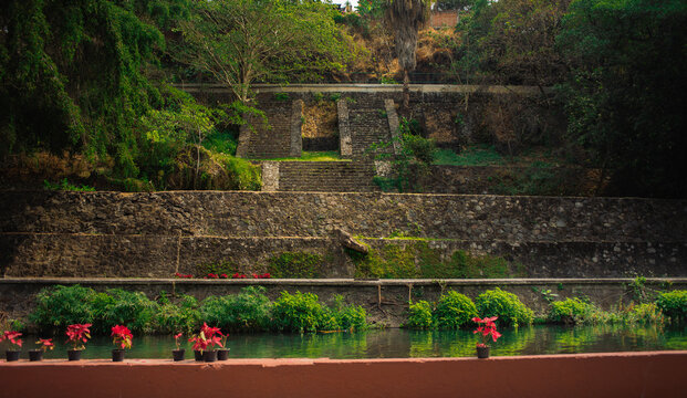 Ancient pyramid standing beside a calm river framed by vibrant poinsettia plants inside Chapultepec Park, Cuernavaca, a beloved photography spot and cultural landmark for tourists and local visitors