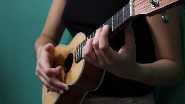 Close-up of a woman playing a wooden ukulele against a teal background