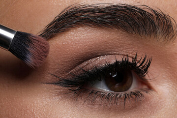 Naklejka premium Applying eye shadow with brush onto woman's face, closeup