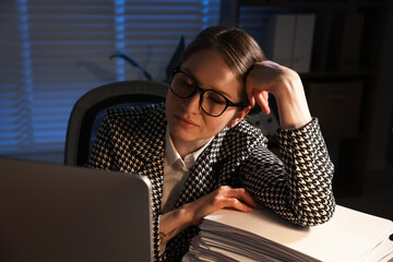 Workaholic. Overwhelmed woman with stack of documents and computer indoors at night © New Africa