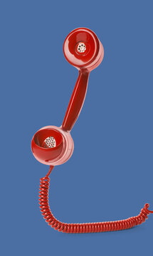 Red telephone handset with cord on blue background. Hotline concept