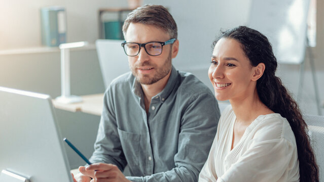 Smiling Young Caucasian Man And Woman Collaborating Together While Working On A Project At Modern Office, Focused On Their Task, Engaging In Discussion And Brainstorming Ideas, Business Concept