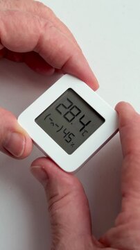 Closeup woman's hands holding digital hygrometer displaying temperature and humidity, small white square sensor, floral