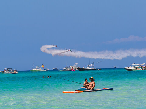 Couple on Paddleboard Fishing While Aerobatic Planes Perform Over Ocean