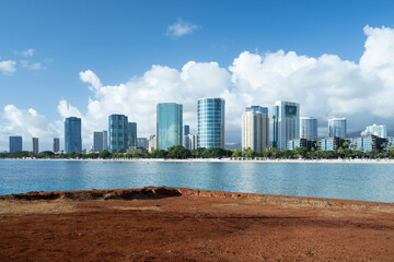 Honolulu city skyline featuring modern high-rise buildings along the coast, stretching against a clear blue ocean, white sands, and a vibrant sky with scattered clouds in Hawaii © Rahman
