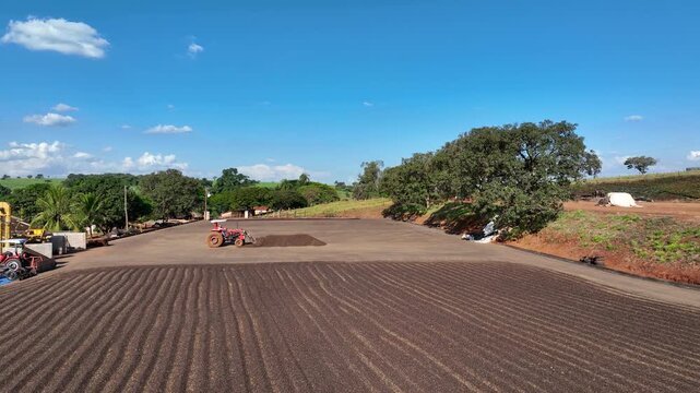 Wide shot of a tractor handling coffee beans on a large drying patio