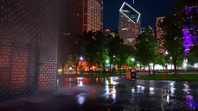 Ground perspective of wet plaza and skyscrapers, Chicago, Illinois. Post rain scene showing glowing glass brick fountain wall and distant illuminated city towers.