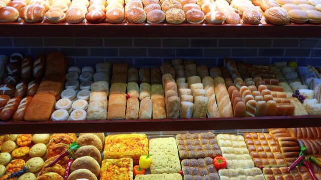 Abundant rows of diverse bread loaves and buns on bakery shelves. A frontal view of a multi tier market display featuring baguettes, burger rolls, and colorful decorated flatbreads.