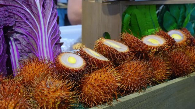 Close-up of rambutan fruit in a wooden crate, Chicago, Illinois. Detailed eye-level view of sliced tropical fruits with white flesh and yellow seeds next to purple cabbage.