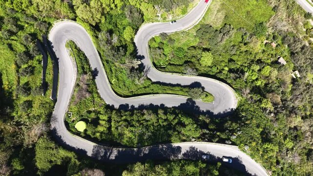 Aerial view of winding mountain roads with sharp hairpin turns snaking through lush green hills and Mediterranean vegetation in Savoca, Sicily, Italy.