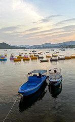 Fototapeta premium Boats docked in a calm bay at sunset with distant mountains and colorful paddle boats