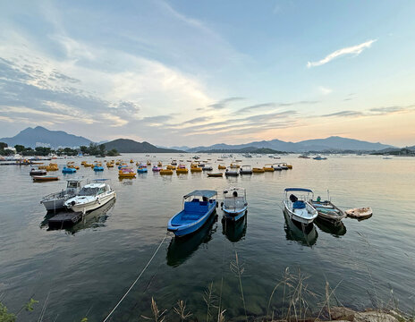 Boats docked in a calm coean at sunset with distant mountains and colorful paddle boats