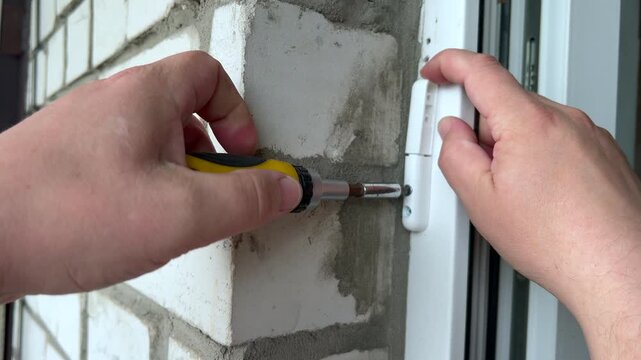 Person repairing window hinge with screwdriver